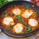a vibrant shakshuka with five poached eggs in a skillet and tomato sauce