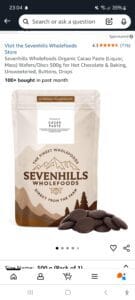 A 500g bag of Sevenhills Wholefoods Organic Cacao Paste is displayed upright, with some round cacao discs scattered in front. The packaging is beige with brown accents and mountain graphics.