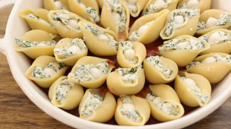 A ceramic dish filled with jumbo pasta shells stuffed with a creamy spinach and ricotta mixture, ready for baking. The dish is placed on a wooden surface.