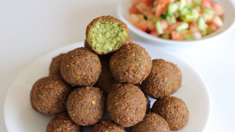 a stack of falafel balls with one bitten ball with a green interior and fresh salad in the background