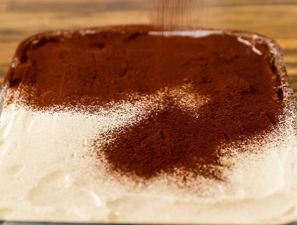 dusing tiramisu with cocoa powder