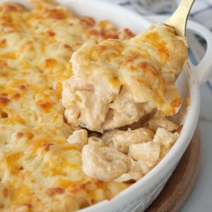 A fork lifts a creamy, cheesy serving of baked macaroni and cheese from a white casserole dish filled with golden, melted cheese on top.
