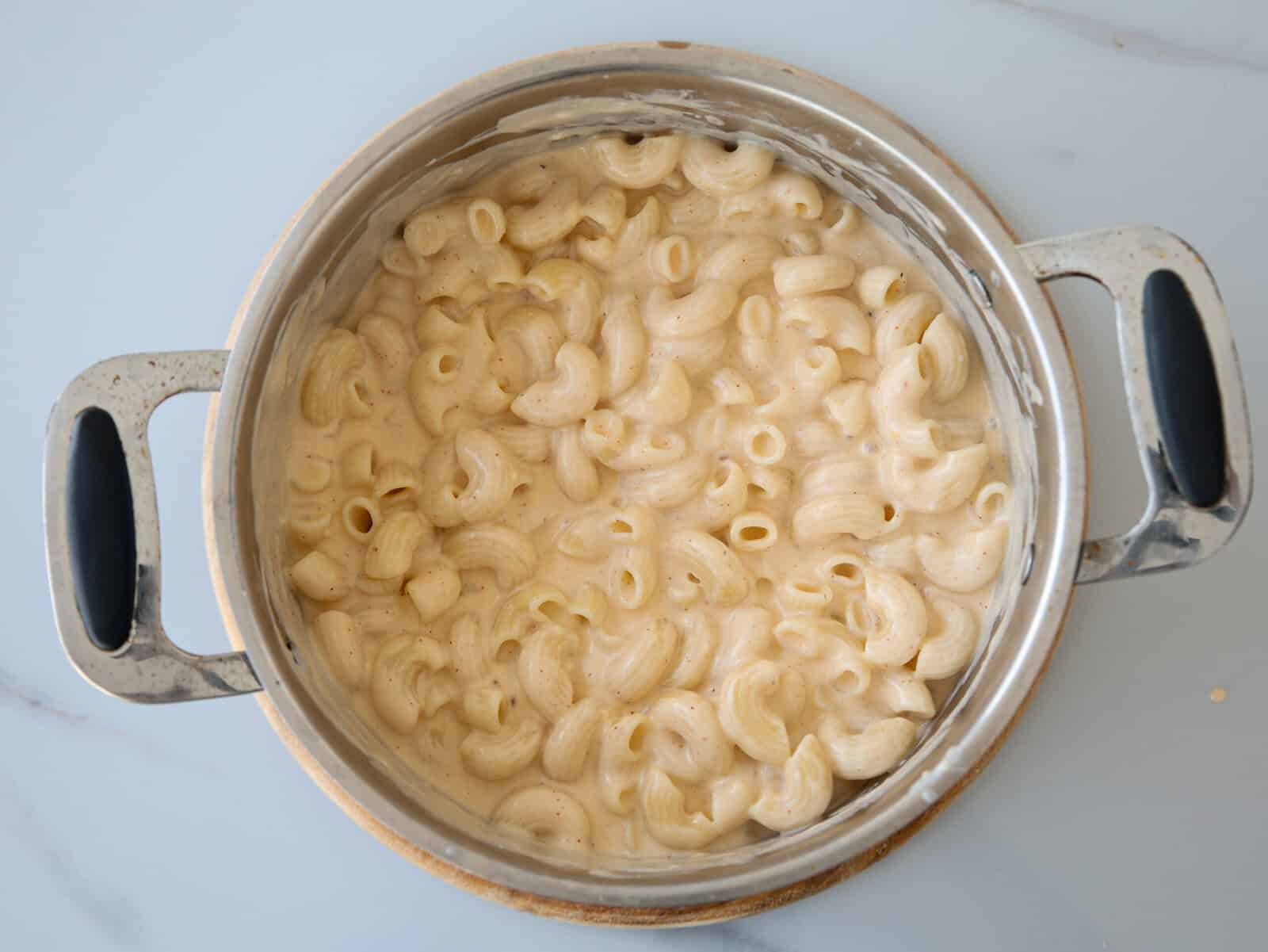 A pot filled with cooked elbow macaroni pasta mixed in a creamy white cheese sauce, sitting on a light-colored surface.