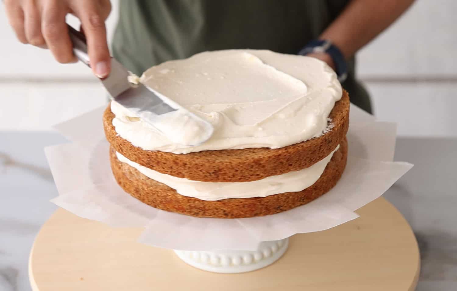 spreading a layer of cream cheese frosting on top of a double layer carrot cake