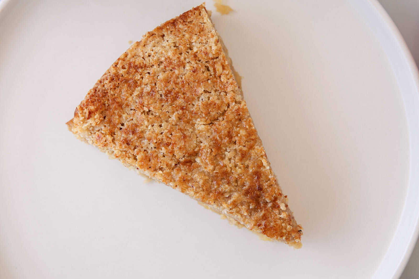 cripsy top of an apple and oatmeal cake on a white clean plate