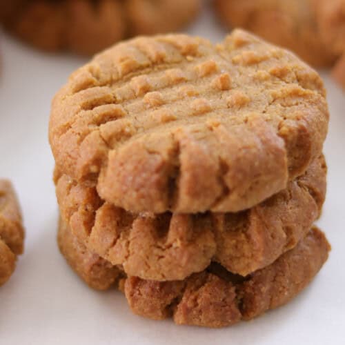 Close-up of rows of freshly baked peanut butter cookies on a baking sheet lined with parchment paper. The cookies have a characteristic crisscross pattern on the tops and are golden brown in color.