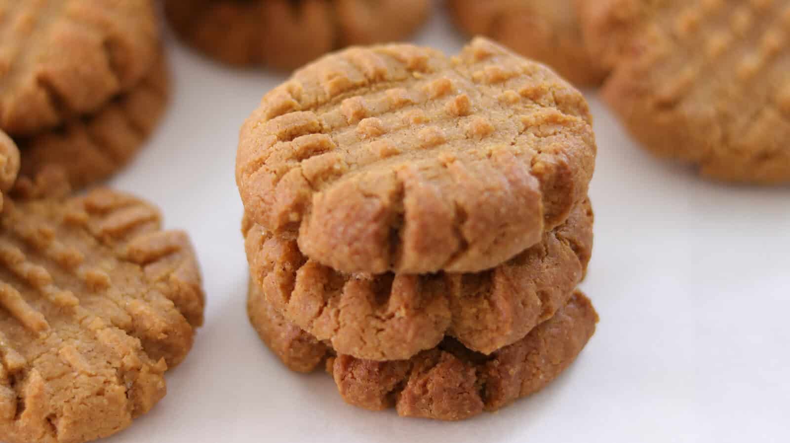 Close-up of rows of freshly baked peanut butter cookies on a baking sheet lined with parchment paper. The cookies have a characteristic crisscross pattern on the tops and are golden brown in color.