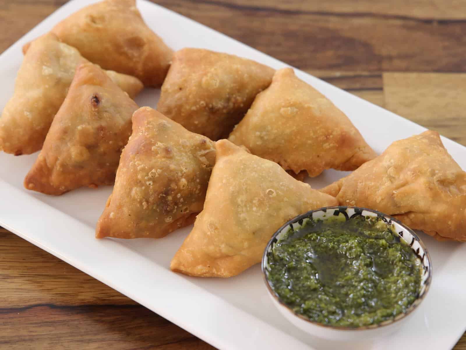 crispy samosa on a plate along side with green sauce