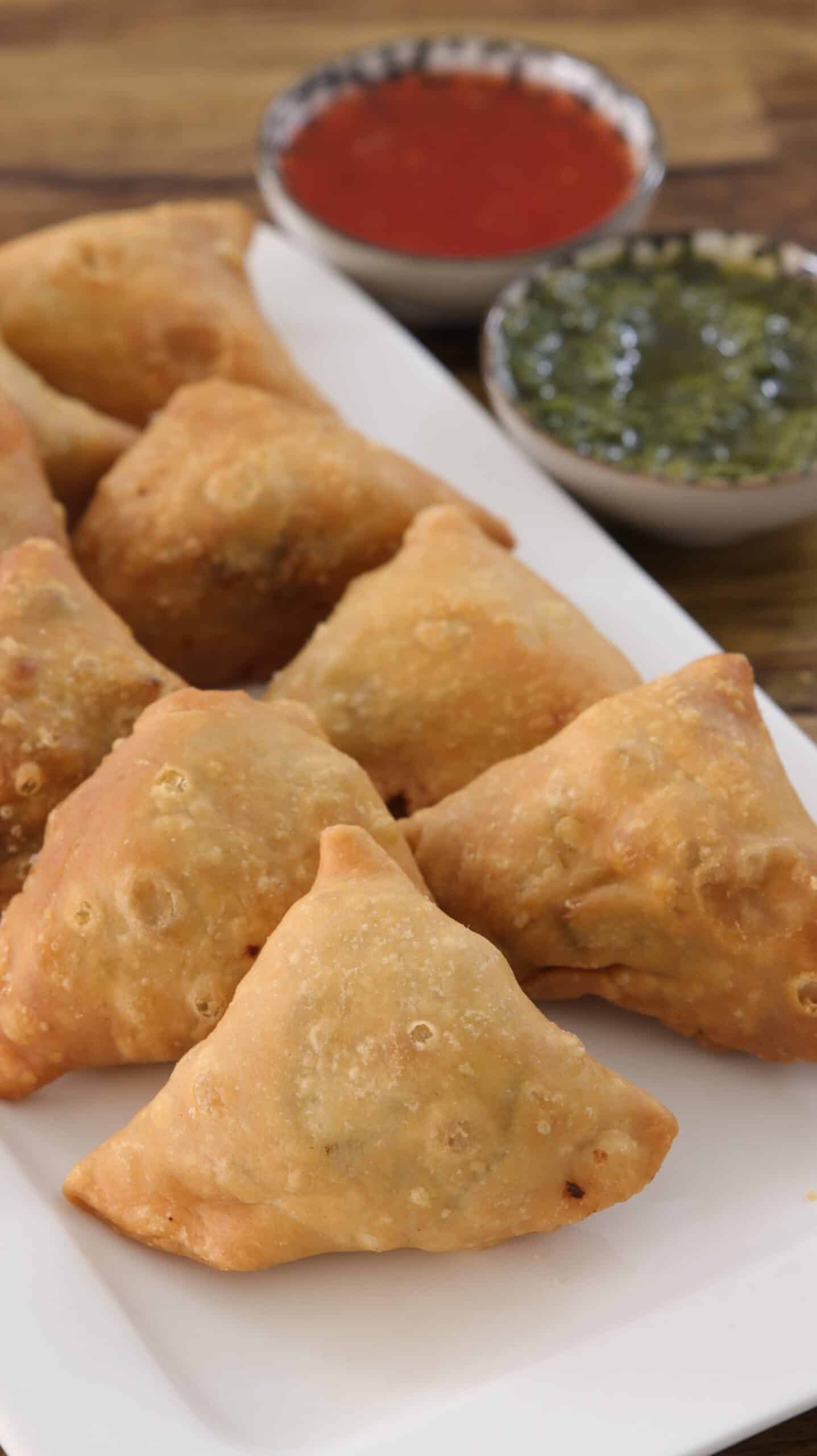 crispy samosas on a white plate with two dipping sauces in the background 