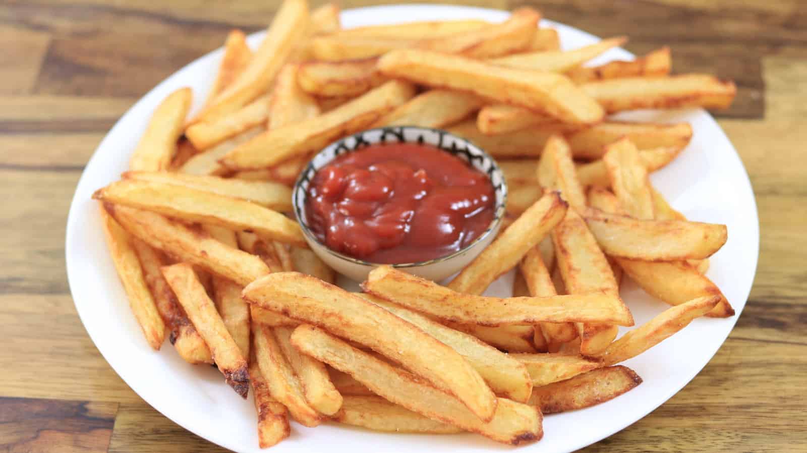 A plate of homemade French fries with a small bowl of ketchup in the center. 