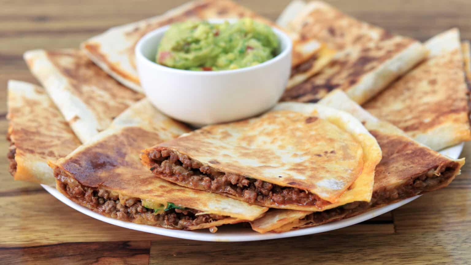 A plate of crispy quesadillas filled with seasoned beef, served with a bowl of fresh guacamole on the side.