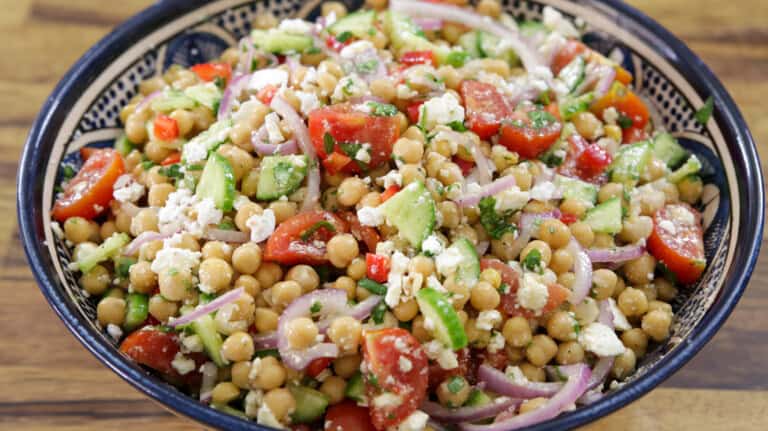 A vibrant chickpea salad in a bowl, featuring chickpeas, chopped tomatoes, cucumbers, red onions, bell peppers, crumbled feta cheese, and fresh herbs, all mixed together. The salad looks fresh and colorful, perfect for a healthy meal.