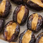 A white rectangular plate holds several dates stuffed with a creamy filling. Nuts are scattered around the dates, adding texture and contrast to the dish.