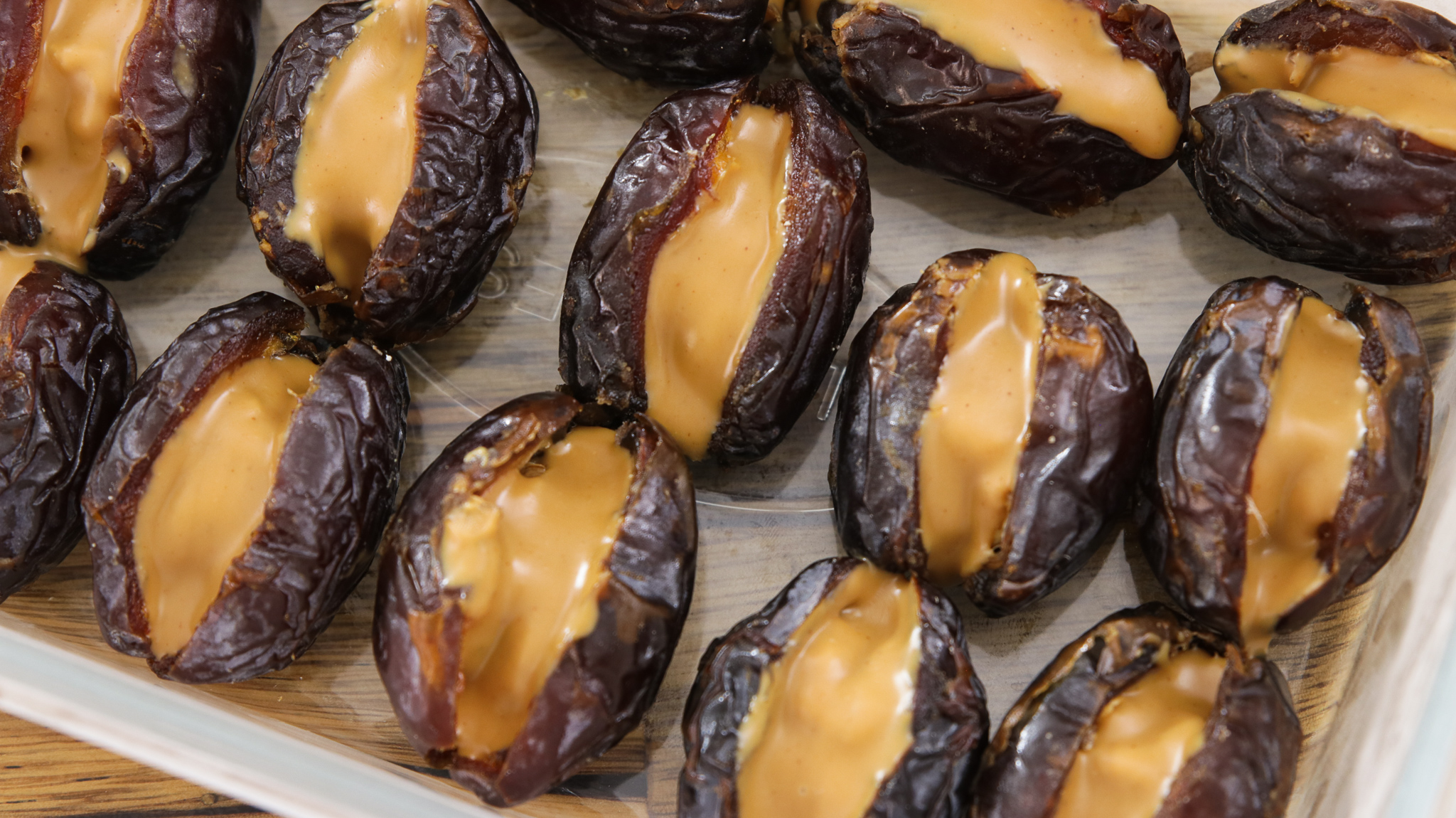 A white rectangular plate holds several dates stuffed with a creamy filling. Nuts are scattered around the dates, adding texture and contrast to the dish.