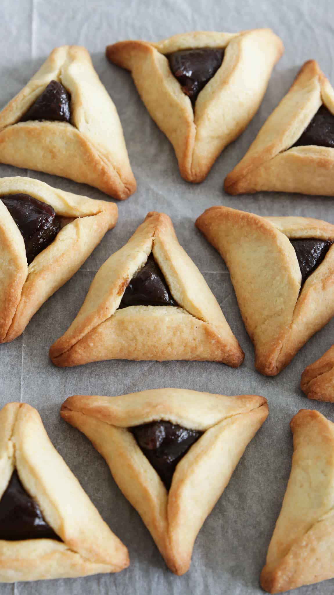 a close up on several Hamantaschen with date filling a baking tray with parchment paper