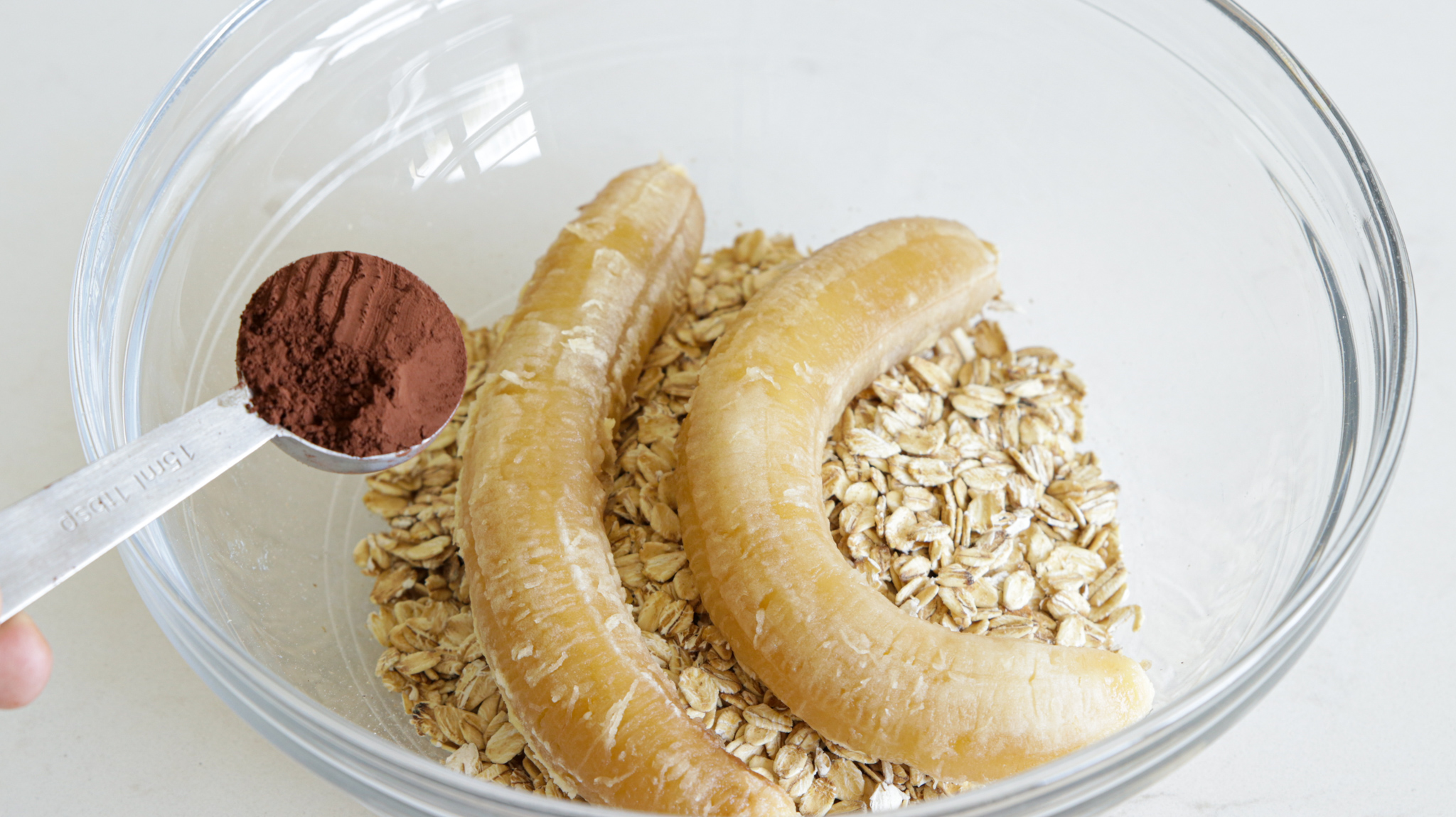 rolled oat, two ripe bananas in a mixing bowl and a tablespoon of cocoa powder has been added