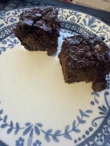 Two pieces of chocolate cake with chocolate chips are placed on a decorative white and blue plate. The texture looks moist and rich, and a keyboard is partly visible in the background.