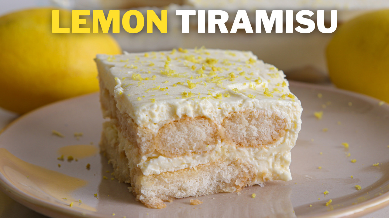 A slice of lemon tiramisu sits on a plate, garnished with grated lemon zest. The background features whole lemons and a blurred view of the full tiramisu dessert. The words "LEMON TIRAMISU" are prominently displayed at the top of the image.