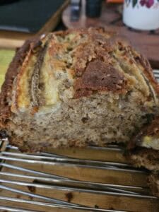 A close-up of a sliced loaf of banana bread on a cooling rack, showing its moist and textured interior with pieces of banana visible on top.