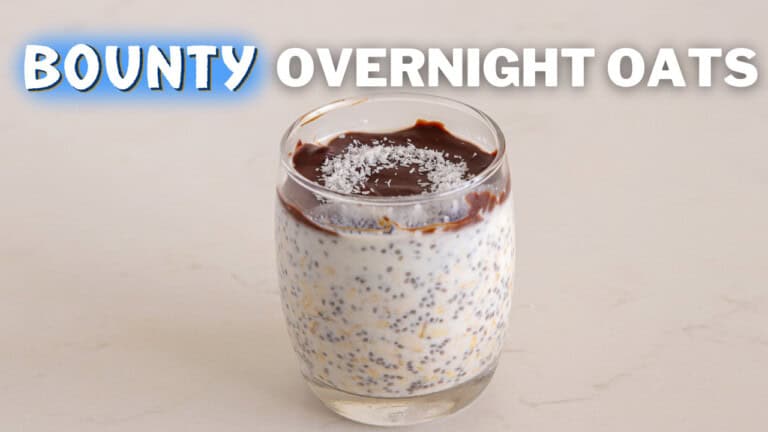 A glass of overnight oats topped with a layer of chocolate and sprinkled with coconut flakes on a white surface. Bold white text above the glass reads "Bounty Overnight Oats.