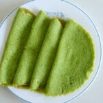 A white plate with four folded green spinach crepes arranged in a fan shape on a light-colored surface.