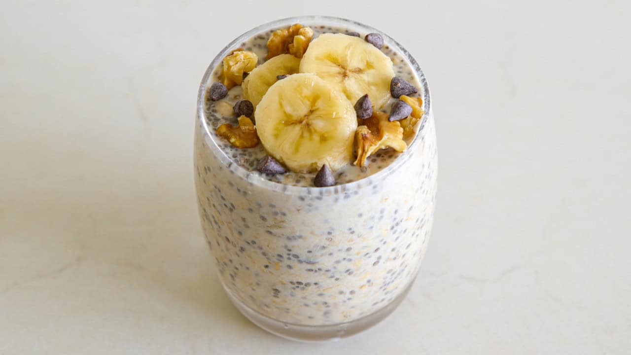 chunkey monkey overnight oats i a glass topped with banana slices, chocolate chips and walnuts