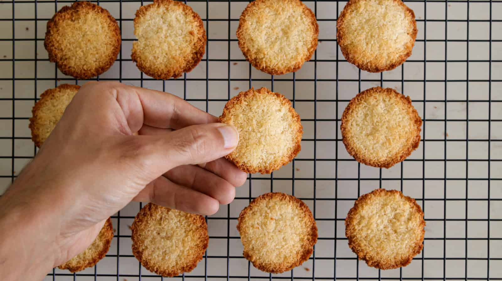 A hand is picking up one of several golden-brown baked goods from a cooling rack. Bold white text at the top reads "2-INGREDIENT.