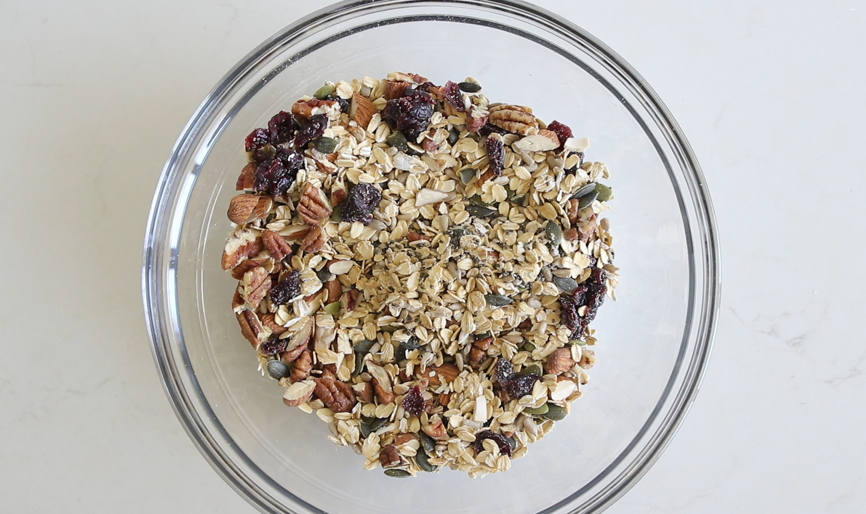 Combine rolled oats, dried fruits, nuts, seeds, and a touch of salt with coconut oil and maple syrup in a bowl.