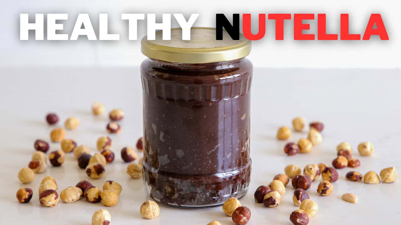 A jar of homemade Nutella sits on a white surface, surrounded by scattered hazelnuts. The text "HEALTHY NUTELLA" is prominently displayed above the jar, with "HEALTHY" in white and "NUTELLA" in red and black.