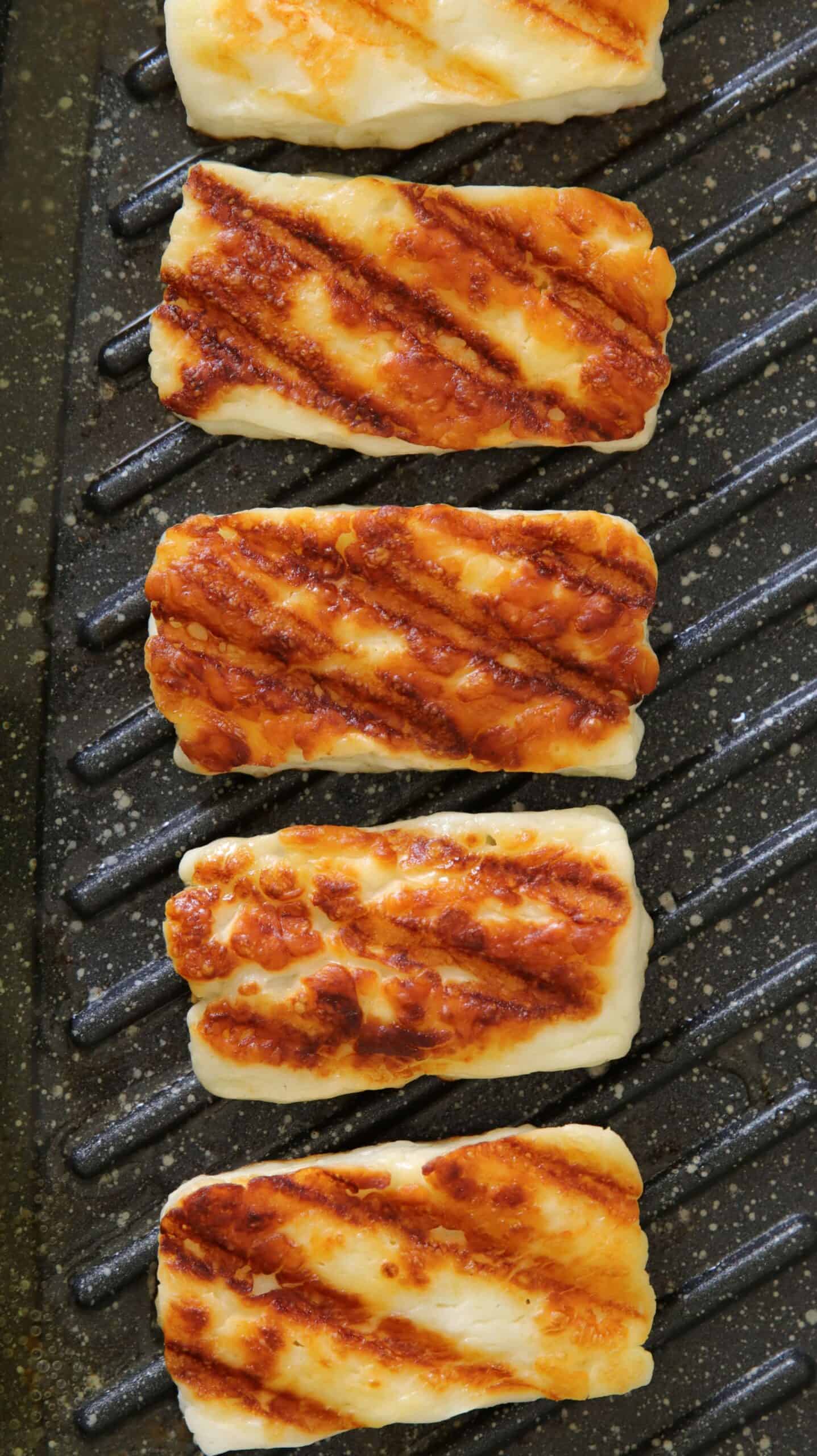 fice slice of halloumi cheese are grilling on a grill pan