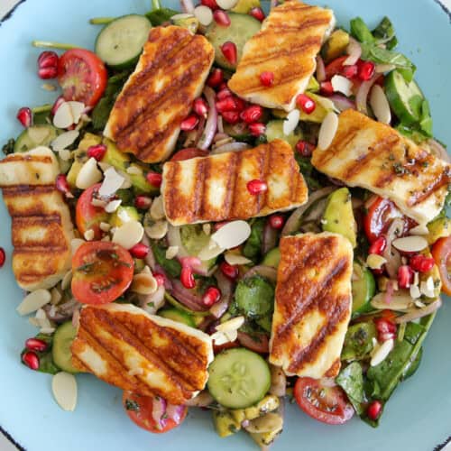 a summer fresh salad with cherry tomatoes, and cucumber topped with grilled halloumi