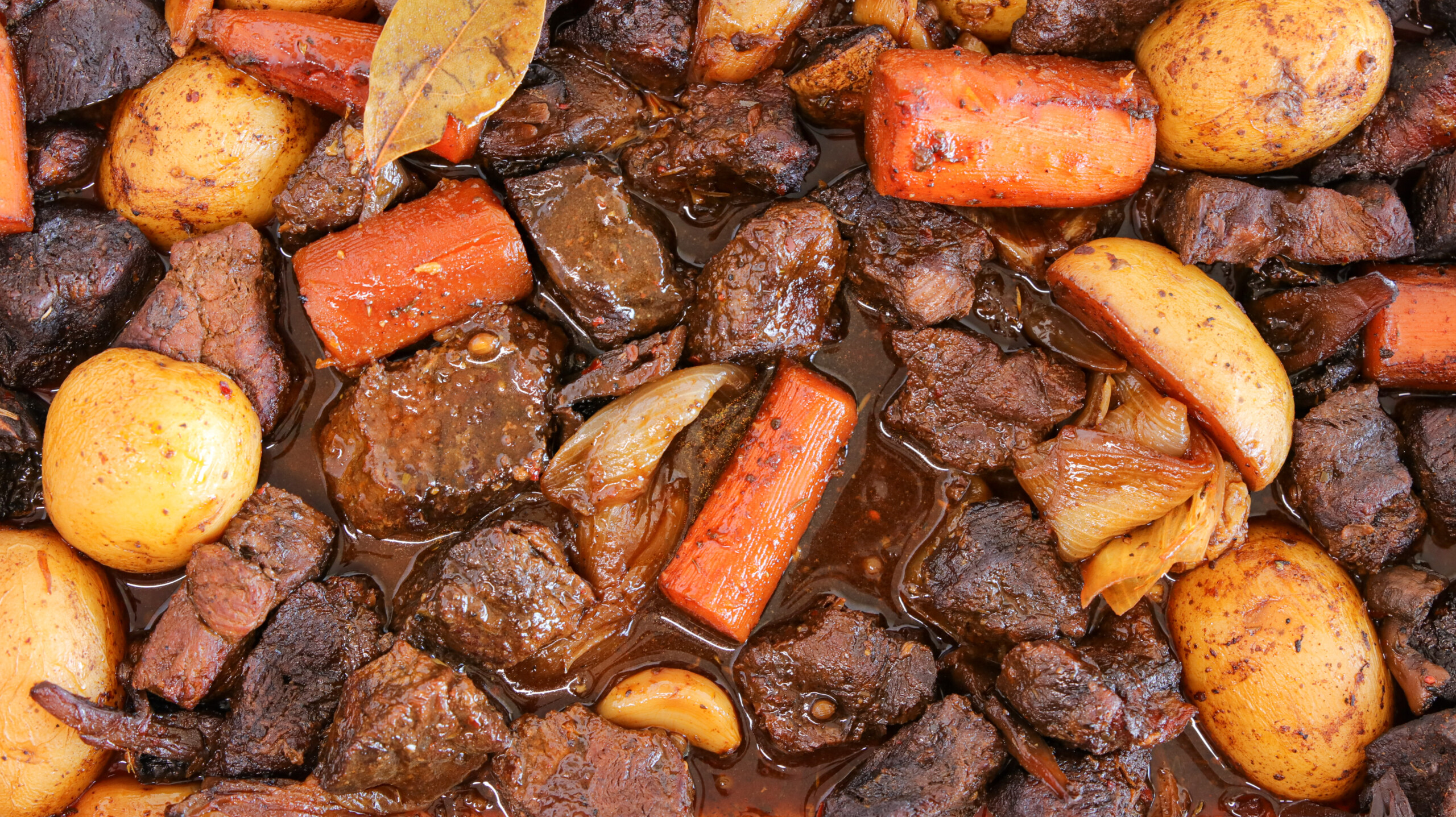 A close-up of a dish labeled "Roasted Beef" featuring chunks of beef, carrots, potatoes, and onions in a rich, dark sauce. The ingredients appear to be well-cooked and seasoned, with the beef looking tender and juicy.