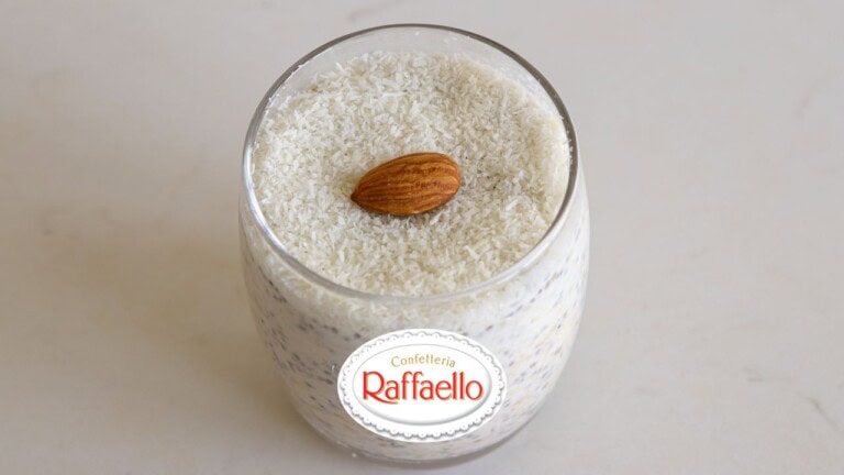 A glass of overnight oats is topped with shredded coconut and an almond. The words "OVERNIGHT OATS" appear above the glass, and a Raffaello logo is positioned to the left.