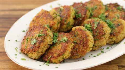 A plate of golden-brown falafel patties garnished with fresh chopped herbs. The falafel is crisp on the outside and served on a white, oval dish, placed on a wooden table.