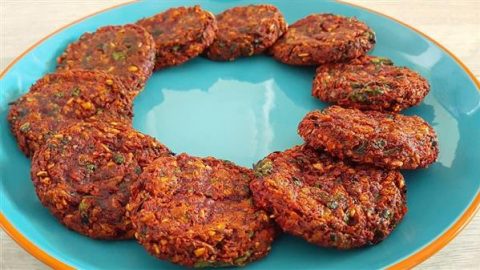 A blue plate holds a neatly arranged ring of orange-brown vegetable fritters. The fritters are evenly spaced, displaying their textured surfaces and hints of green herbs. The plate is set on a light, plain background.