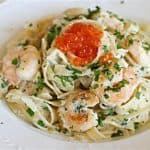 A white plate filled with creamy fettuccine pasta topped with cooked shrimp, garnished with chopped parsley, and a spoonful of bright orange fish roe placed in the center. The pasta and shrimp are well-mixed in a rich, creamy sauce.