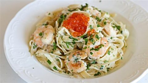 A white plate filled with creamy fettuccine pasta topped with cooked shrimp, garnished with chopped parsley, and a spoonful of bright orange fish roe placed in the center. The pasta and shrimp are well-mixed in a rich, creamy sauce.