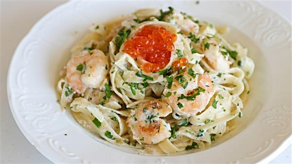 A white plate filled with creamy fettuccine pasta topped with cooked shrimp, garnished with chopped parsley, and a spoonful of bright orange fish roe placed in the center. The pasta and shrimp are well-mixed in a rich, creamy sauce.