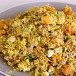 A plate of vibrant quinoa salad. The dish includes quinoa mixed with chunks of butternut squash, finely chopped herbs, small pieces of chicken, and crumbled feta cheese. The salad appears well-seasoned and garnished with fresh herbs.