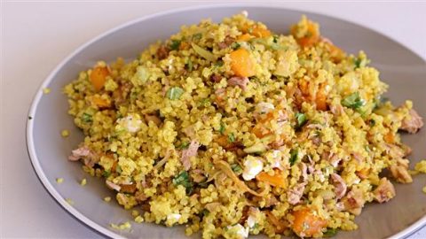 A plate of vibrant quinoa salad. The dish includes quinoa mixed with chunks of butternut squash, finely chopped herbs, small pieces of chicken, and crumbled feta cheese. The salad appears well-seasoned and garnished with fresh herbs.