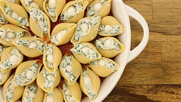 A ceramic dish filled with jumbo pasta shells stuffed with a creamy spinach and ricotta mixture, ready for baking. The dish is placed on a wooden surface.