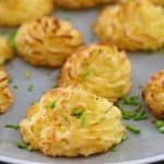 A plate of golden-brown duchess potatoes garnished with finely chopped chives. The potatoes are piped into neat, swirled mounds, showcasing a crispy exterior with a fluffy interior. They are artfully arranged on the plate, ready to be served.