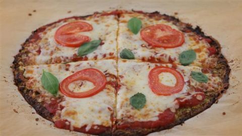 A homemade pizza topped with melted cheese, tomato sauce, tomato slices, and basil leaves. The pizza is partially sliced into four pieces and has a thin, slightly crispy-looking crust.