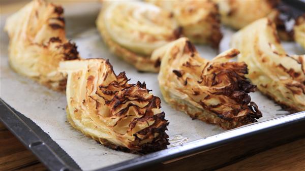 Golden-brown roasted cabbage wedges on a baking sheet. The edges are slightly charred, giving a crispy texture, while the inner portions remain tender. The tray rests on a wooden surface.