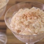 Two glass dishes filled with creamy rice pudding are pictured. The rice pudding is topped with a sprinkle of cinnamon, and the dishes are set on a wooden surface, giving the scene a cozy and rustic feel.