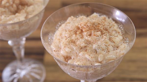 Two glass dishes filled with creamy rice pudding are pictured. The rice pudding is topped with a sprinkle of cinnamon, and the dishes are set on a wooden surface, giving the scene a cozy and rustic feel.