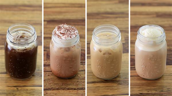 Four mason jars filled with different iced coffee drinks are lined up on a wooden surface. From left to right: black iced coffee, iced coffee with cocoa powder, iced coffee with milk, and iced coffee topped with a scoop of vanilla ice cream.