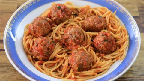 A dish of spaghetti and meatballs in tomato sauce is served on a plate with a blue and white rim. The vibrant red sauce coats the pasta and meatballs, and the dish is placed on a wooden surface.