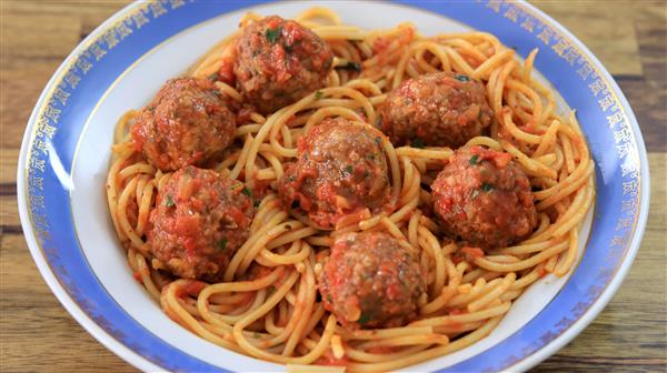 A dish of spaghetti and meatballs in tomato sauce is served on a plate with a blue and white rim. The vibrant red sauce coats the pasta and meatballs, and the dish is placed on a wooden surface.