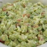 A close-up of a bowl filled with creamy avocado egg salad. The dish contains chopped avocado, hard-boiled eggs, tomatoes, and a creamy dressing, all mixed together. The white bowl has a decorative pattern on the rim.